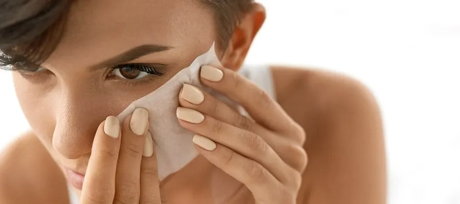 Closeup of woman holding makeup blotting sheet to her cheek.